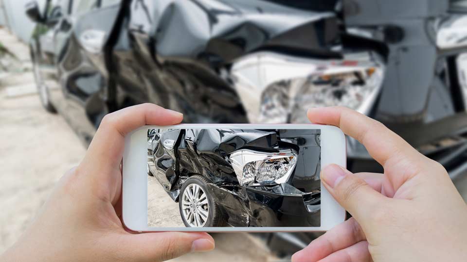 Unfallwagenankauf Saarbrücken: Unfallschaden an einem Auto wird mit dem Smartphone fotografiert.